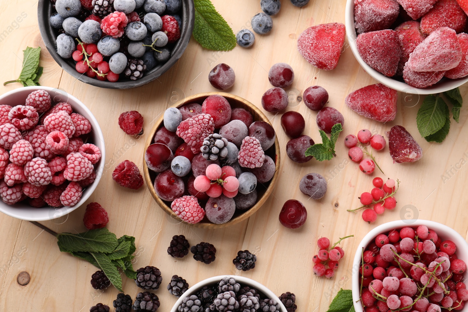 Photo of Different ripe frozen berries and mint leaves on light wooden table, flat lay