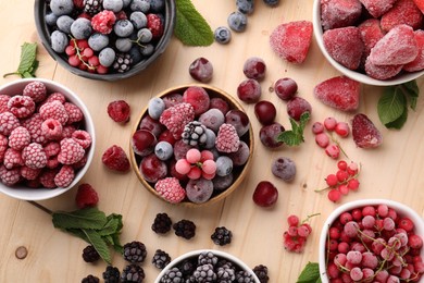 Photo of Different ripe frozen berries and mint leaves on light wooden table, flat lay