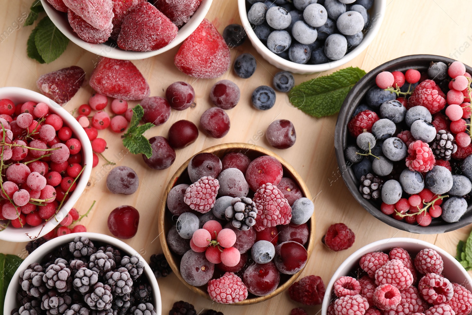 Photo of Different ripe frozen berries and mint leaves on light wooden table, flat lay