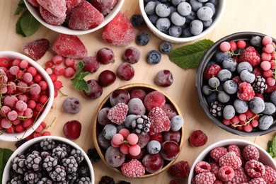 Photo of Different ripe frozen berries and mint leaves on light wooden table, flat lay