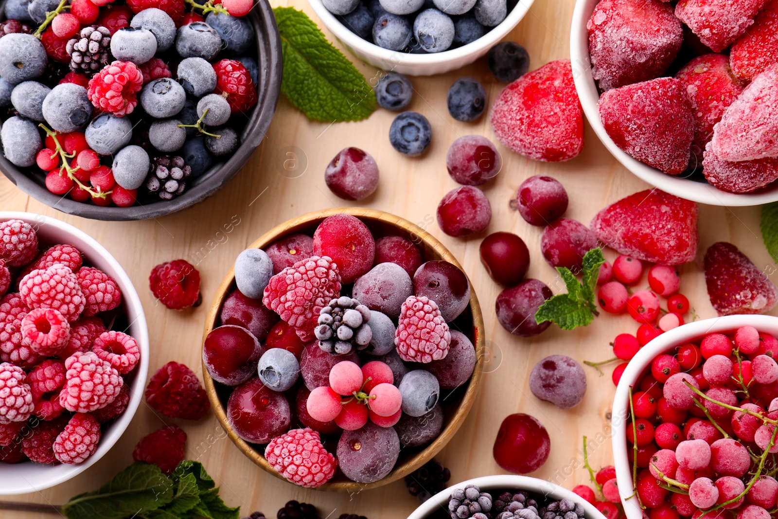 Photo of Different ripe frozen berries and mint leaves on light wooden table, flat lay