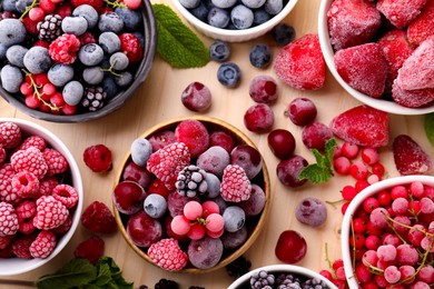 Photo of Different ripe frozen berries and mint leaves on light wooden table, flat lay