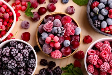 Photo of Different ripe frozen berries and mint leaves on light wooden table, flat lay