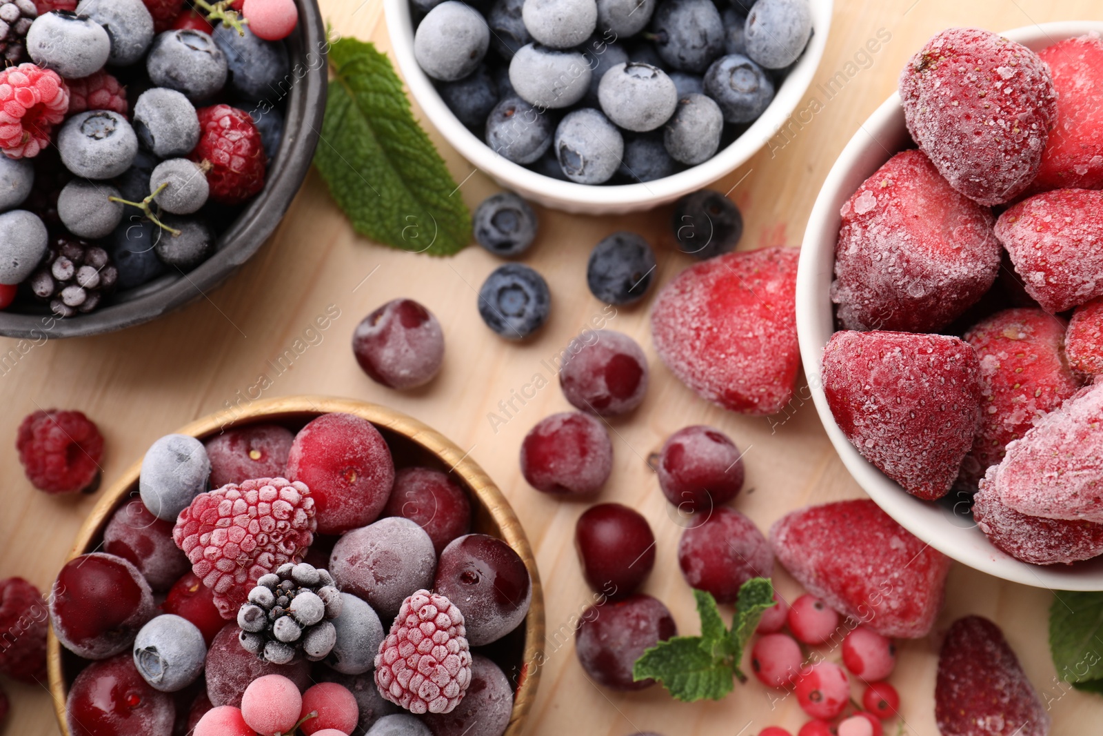 Photo of Different ripe frozen berries and mint leaves on light wooden table, flat lay