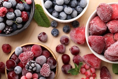 Photo of Different ripe frozen berries and mint leaves on light wooden table, flat lay