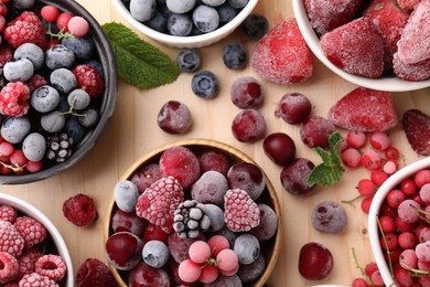 Photo of Different ripe frozen berries and mint leaves on light wooden table, flat lay