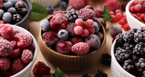 Photo of Different ripe frozen berries and mint leaves on light wooden table, closeup