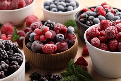 Photo of Different ripe frozen berries and mint leaves on light wooden table, closeup