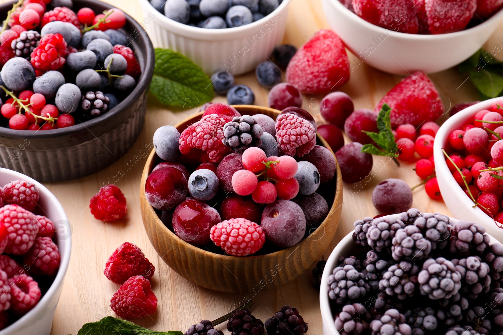 Photo of Different ripe frozen berries and mint leaves on light wooden table, closeup