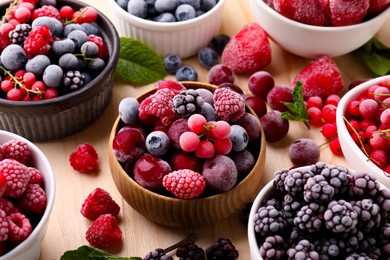 Photo of Different ripe frozen berries and mint leaves on light wooden table, closeup