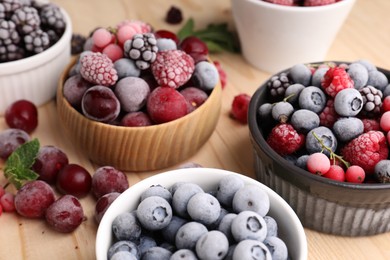 Photo of Different ripe frozen berries and mint leaves on light wooden table, closeup