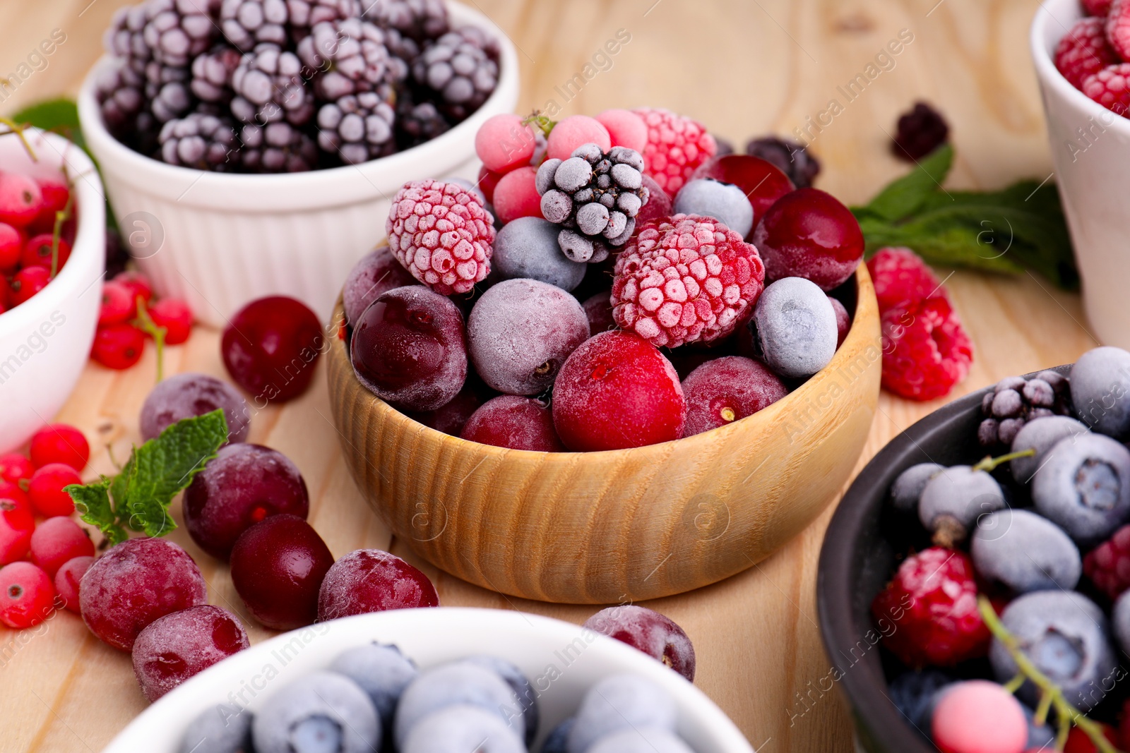 Photo of Different ripe frozen berries and mint leaves on light wooden table, closeup