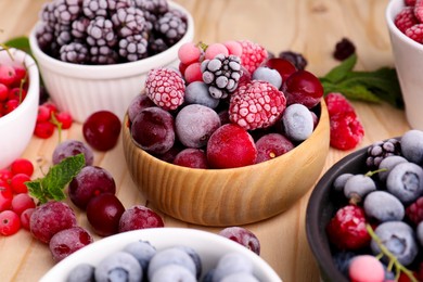 Photo of Different ripe frozen berries and mint leaves on light wooden table, closeup