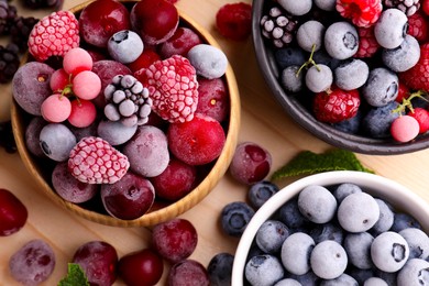 Photo of Different ripe frozen berries and mint leaves on light wooden table, flat lay