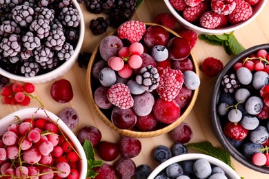 Photo of Different ripe frozen berries and mint leaves on light wooden table, flat lay