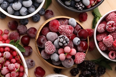 Photo of Different ripe frozen berries and mint leaves on light wooden table, flat lay