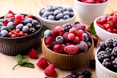 Photo of Different ripe frozen berries and mint leaves on light wooden table, closeup