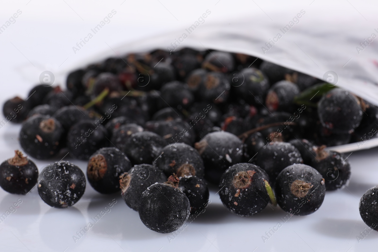 Photo of Ripe frozen black currants in open zipper bag on mirror surface against white background, closeup