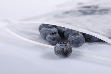 Photo of Ripe frozen blueberries in open zipper bag on white mirror surface, closeup