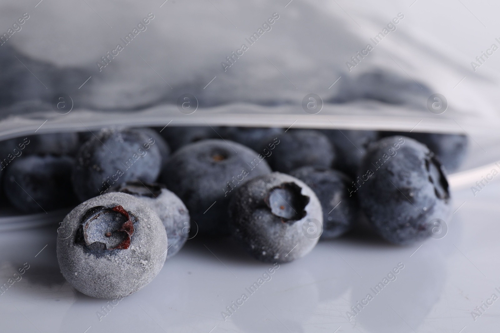 Photo of Ripe frozen blueberries in open zipper bag on white mirror surface, closeup