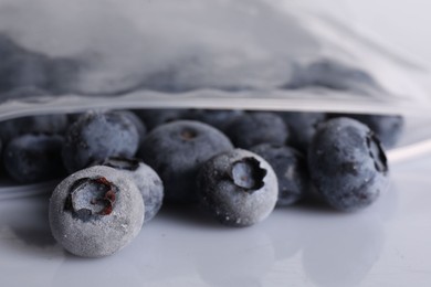 Photo of Ripe frozen blueberries in open zipper bag on white mirror surface, closeup