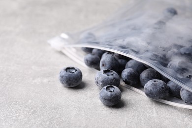 Photo of Ripe frozen blueberries in open zipper bag on grey textured table, closeup