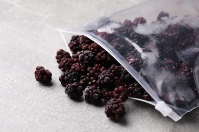 Photo of Ripe frozen blackberries in open zipper bag on grey textured table, closeup