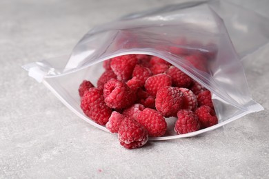 Photo of Ripe frozen raspberries in open zipper bag on grey textured table, closeup