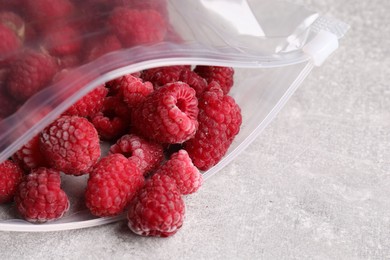 Photo of Ripe frozen raspberries in open zipper bag on grey textured table, closeup