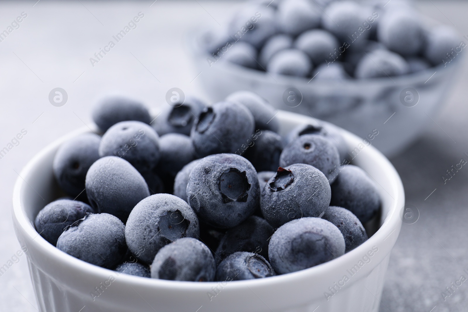 Photo of Ripe frozen blueberries in bowl on grey table, closeup