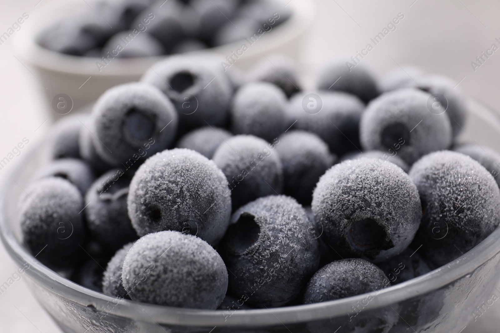 Photo of Ripe frozen blueberries in bowl on grey table, closeup