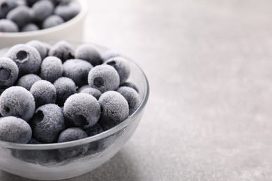 Photo of Ripe frozen blueberries in bowl on grey textured table, closeup. Space for text