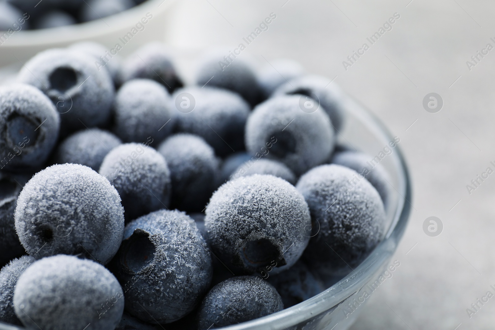 Photo of Ripe frozen blueberries in bowl on blurred light grey background, closeup