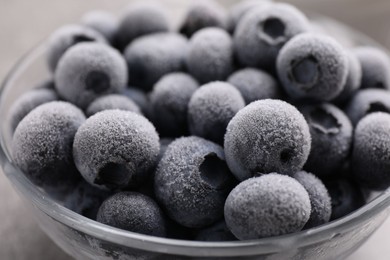 Photo of Ripe frozen blueberries in bowl on grey table, closeup