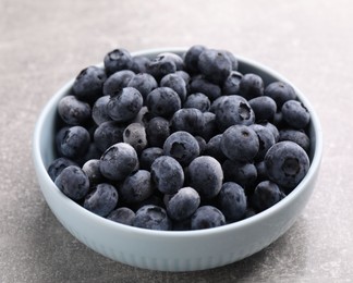 Photo of Ripe frozen blueberries in bowl on grey textured table, closeup