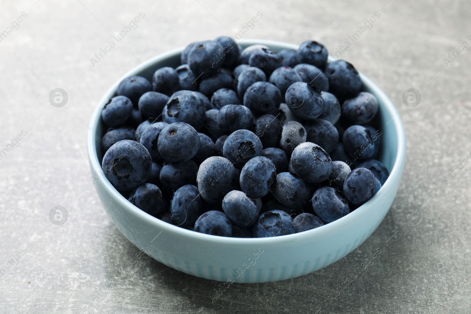 Photo of Ripe frozen blueberries in bowl on grey textured table, closeup