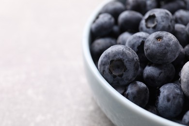 Photo of Ripe frozen blueberries in bowl on light grey table, closeup. Space for text
