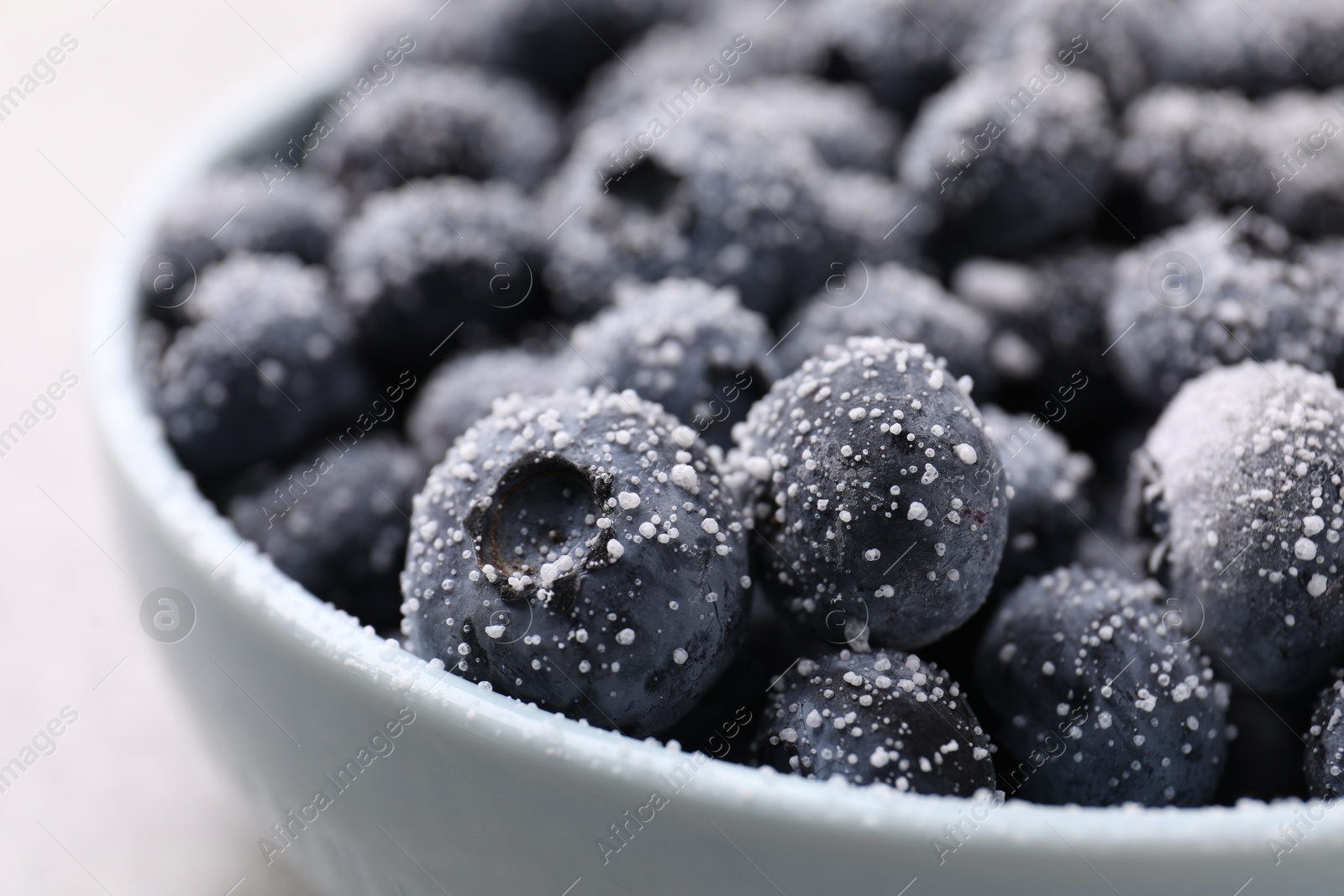Photo of Ripe frozen blueberries in bowl on blurred light background, closeup
