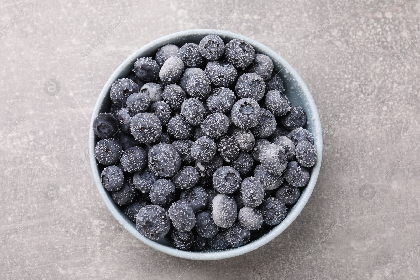 Photo of Ripe frozen blueberries in bowl on grey textured table, top view