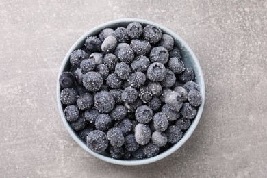 Photo of Ripe frozen blueberries in bowl on grey textured table, top view