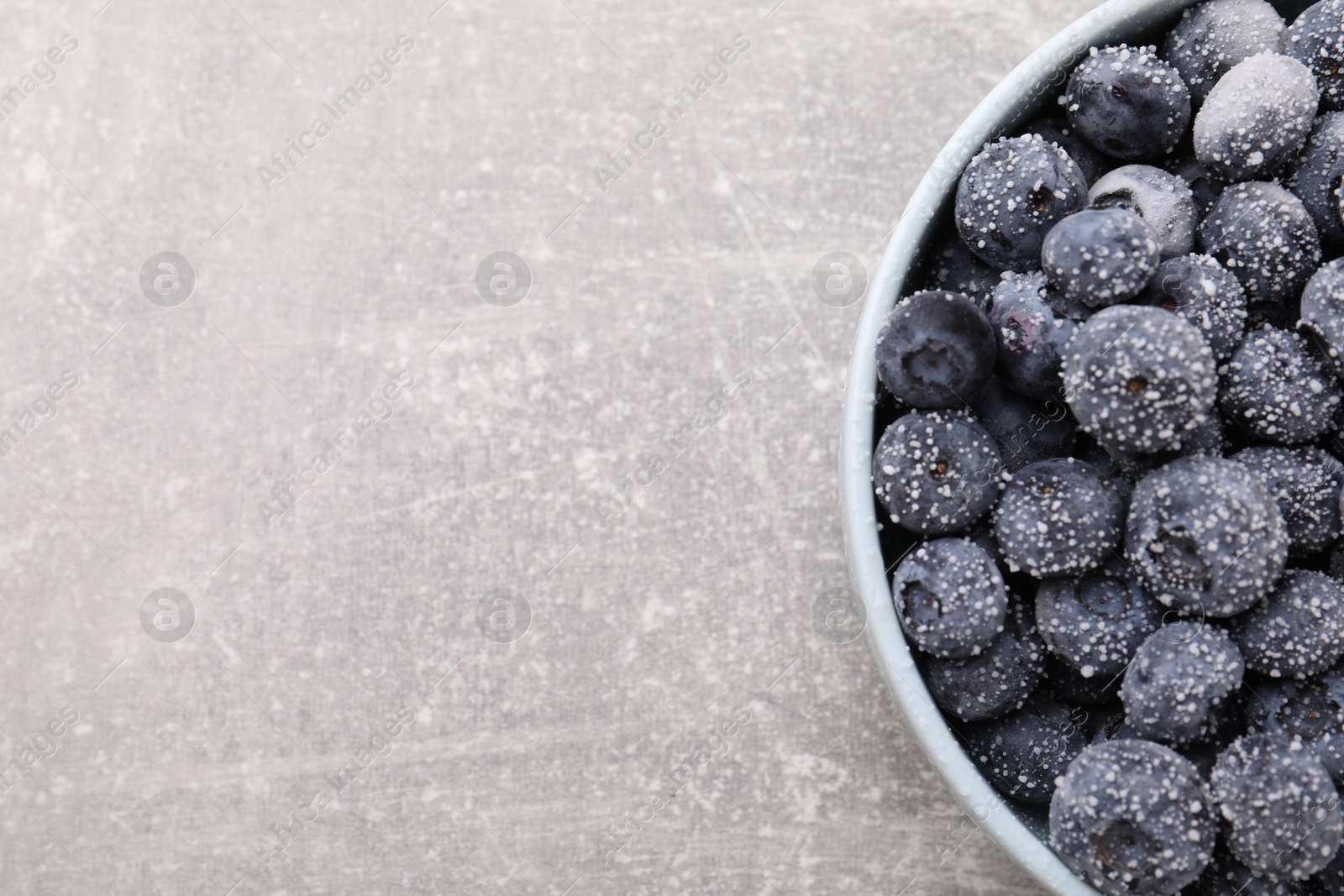 Photo of Ripe frozen blueberries in bowl on grey textured table, top view. Space for text
