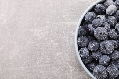 Photo of Ripe frozen blueberries in bowl on grey textured table, top view. Space for text
