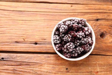 Photo of Ripe frozen blackberries in bowl on wooden table, top view. Space for text