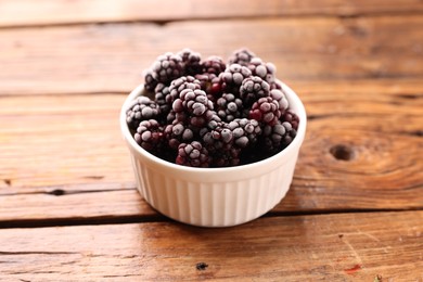 Photo of Ripe frozen blackberries in bowl on wooden table, closeup