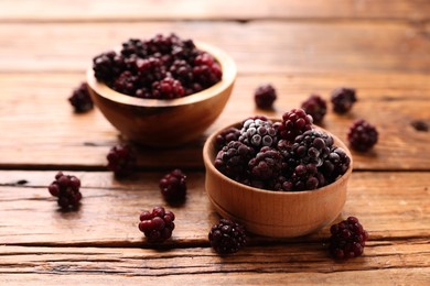 Photo of Ripe frozen blackberries in bowls on wooden table, closeup
