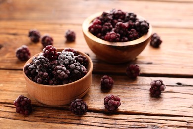 Photo of Ripe frozen blackberries in bowls on wooden table, closeup