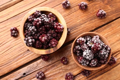 Photo of Ripe frozen blackberries and bowls on wooden table, flat lay