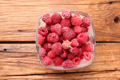 Photo of Ripe frozen raspberries in bowl on wooden table, top view
