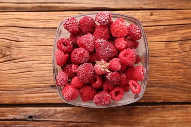 Photo of Ripe frozen raspberries in bowl on wooden table, top view