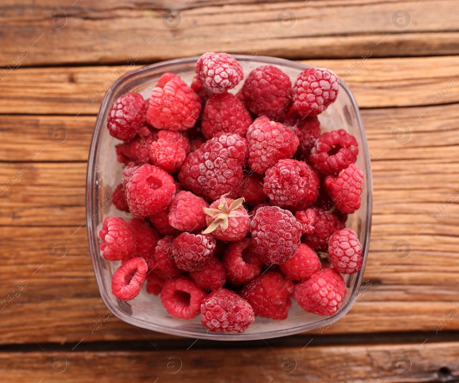 Photo of Ripe frozen raspberries in bowl on wooden table, top view